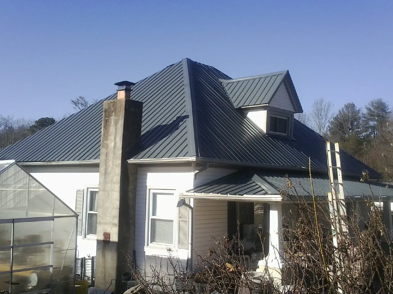 Dark blue standing seam metal roof on a white farmhouse with dormer — Slate & Tile Roof Repair by Roofing Brothers in Bridgehampton