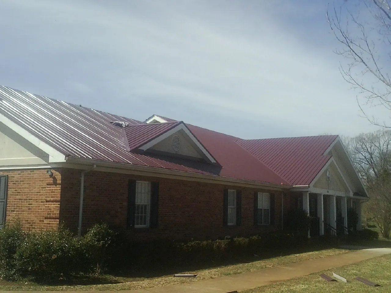 Red metal roof with gabled entries on a long brick building, from a Hail Damage Roof Repair job in Bridgehampton