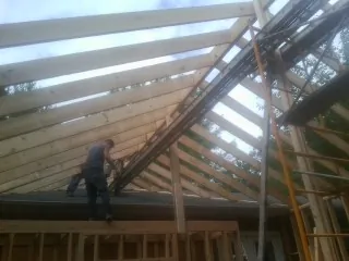 Rafters going up over a new addition with a worker on the wall in Bridgehampton