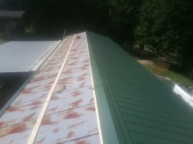 Old rusted panels beside newly installed green metal roofing — Wind Damage Roof Repair by Roofing Brothers in Bridgehampton