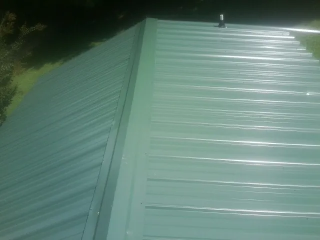 New green metal panels meeting at the ridge of a roof — Flat Roof Repair work by our crew in Bridgehampton